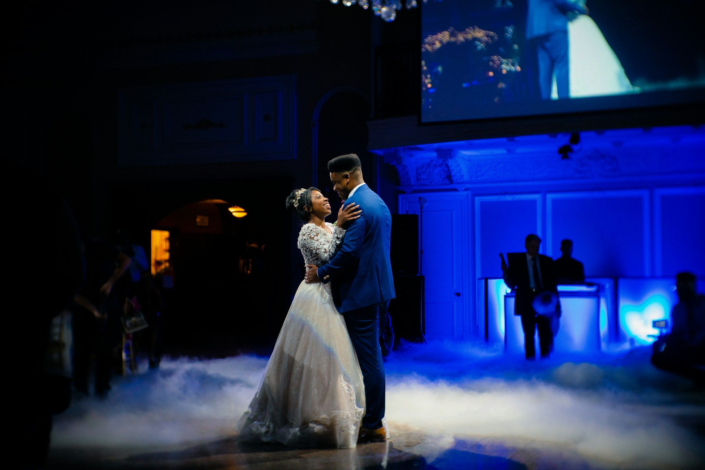 Novios bailando su primer baile sobre humo bajo, con luz azul de fondo